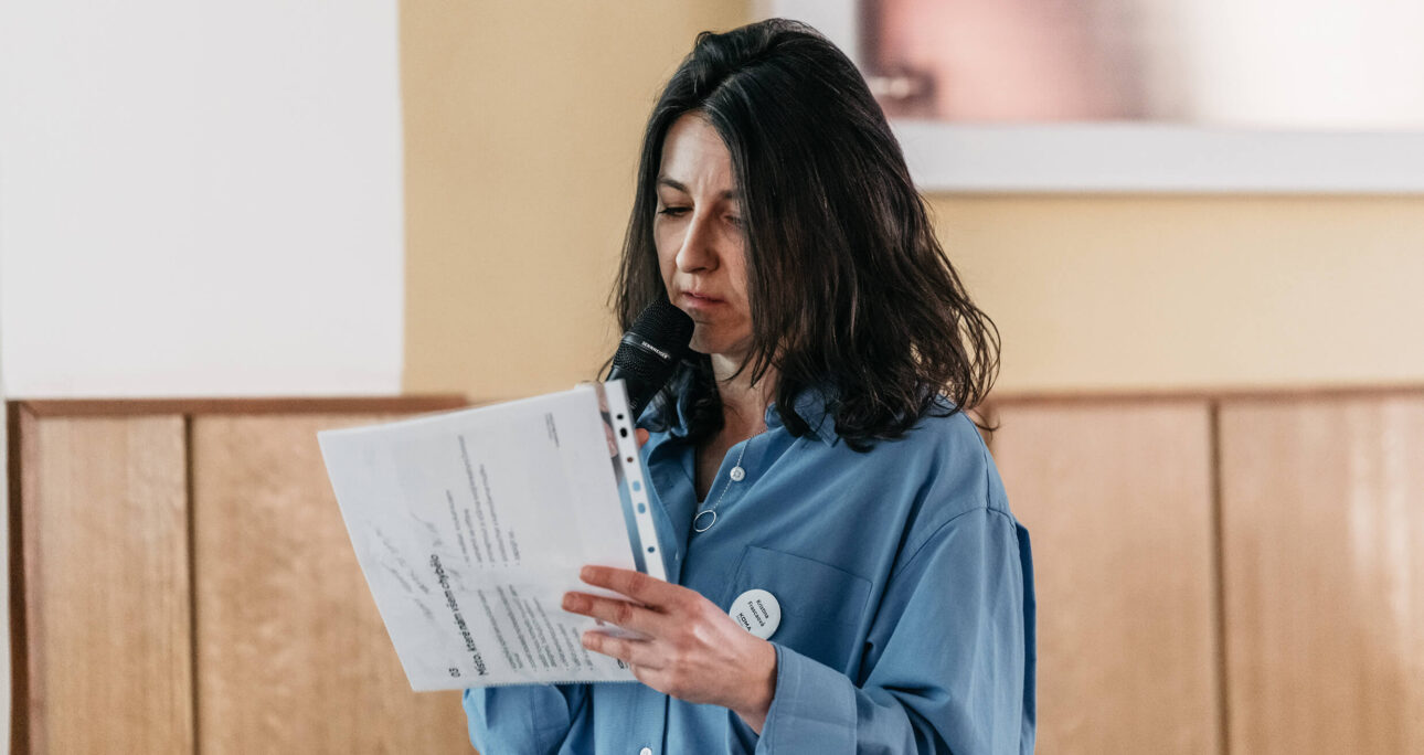 Žena čte z papíru mikrofonem.